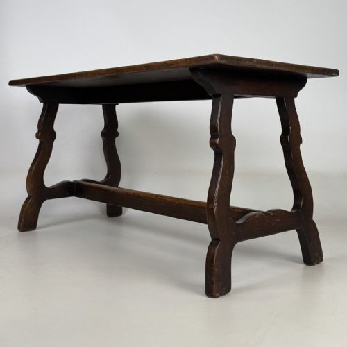 fig 5. A dark brown oak low coffee table featuring a rectangular plank top supported by shaped trestle end legs joined by a low central stretcher.