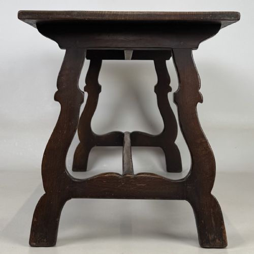 fig 6. A dark brown oak low coffee table featuring a rectangular plank top supported by shaped trestle end legs joined by a low central stretcher.