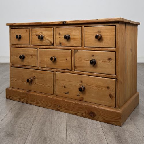 fig 1. A 20th-century pine chest of drawers featuring nine multi-sized drawers with dark turned wooden knobs arranged on a solid plinth base.