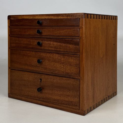 fig 1. An early 20th-century mahogany tabletop cabinet featuring five graduated drawers with dark round pull handles and a keyhole on the lowest drawer.