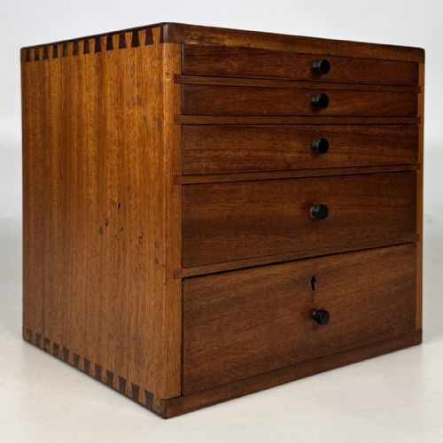 fig 7. An early 20th-century mahogany tabletop cabinet featuring five graduated drawers with dark round pull handles and a keyhole on the lowest drawer.
