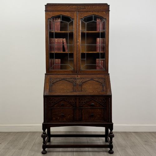 fig 1. A dark Jacobean style oak bureau bookcase with twin leaded glass upper doors, carved fall-front desk, two lower drawers, and turned legs.