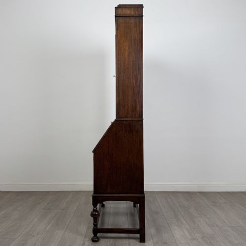 fig 4. A dark Jacobean style oak bureau bookcase with twin leaded glass upper doors, carved fall-front desk, two lower drawers, and turned legs.