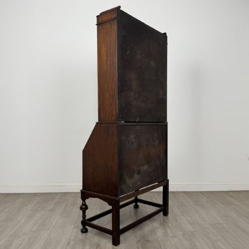 fig 5. A dark Jacobean style oak bureau bookcase with twin leaded glass upper doors, carved fall-front desk, two lower drawers, and turned legs.