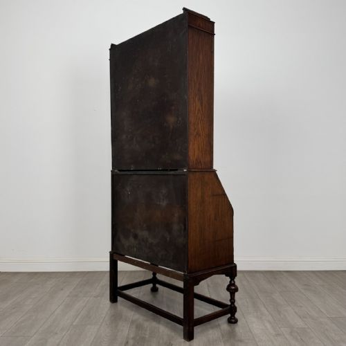 fig 7. A dark Jacobean style oak bureau bookcase with twin leaded glass upper doors, carved fall-front desk, two lower drawers, and turned legs.