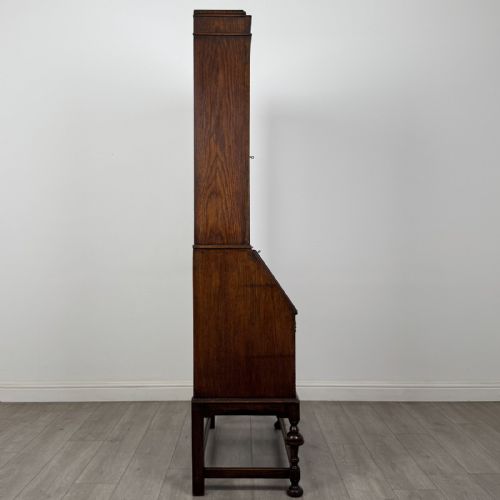 fig 8. A dark Jacobean style oak bureau bookcase with twin leaded glass upper doors, carved fall-front desk, two lower drawers, and turned legs.