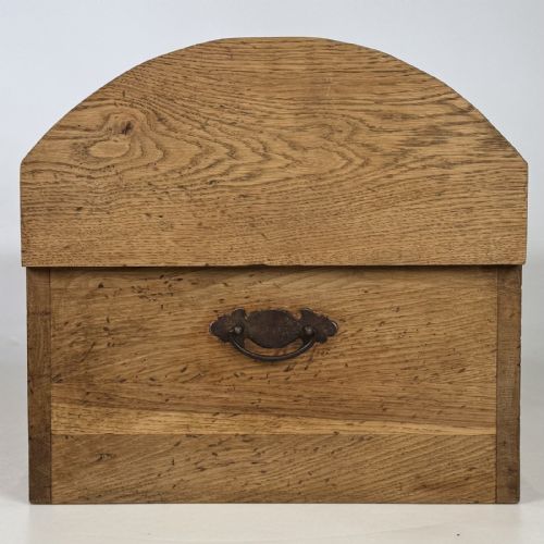 fig 6. A small light oak storage chest featuring a curved domed lid, metal stud details along the side edges, and a central wooden knob on the front.