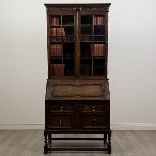 fig 1. A dark oak bureau bookcase with upper glazed doors, a fall-front desk flap, lower drawers, and turned barley twist legs.