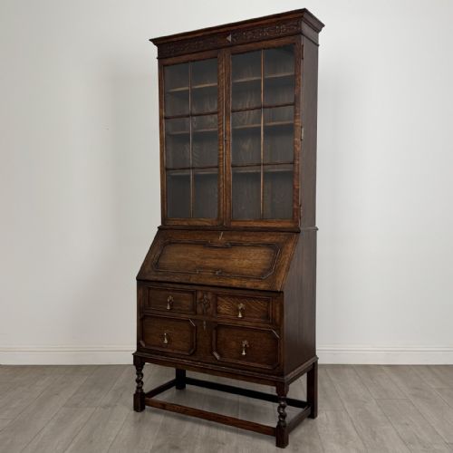 fig 2. A dark oak bureau bookcase with upper glazed doors, a fall-front desk flap, lower drawers, and turned barley twist legs.