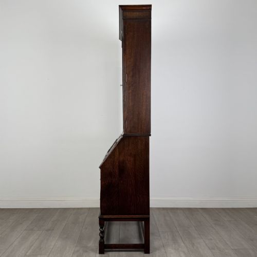 fig 3. A dark oak bureau bookcase with upper glazed doors, a fall-front desk flap, lower drawers, and turned barley twist legs.