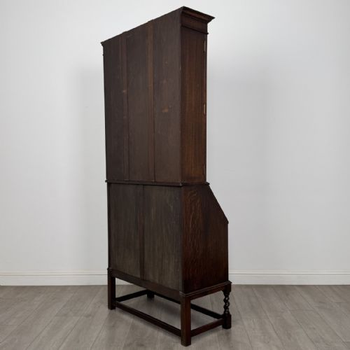 fig 6. A dark oak bureau bookcase with upper glazed doors, a fall-front desk flap, lower drawers, and turned barley twist legs.