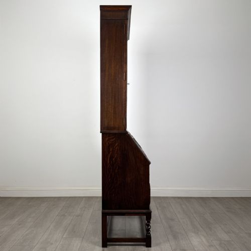 fig 7. A dark oak bureau bookcase with upper glazed doors, a fall-front desk flap, lower drawers, and turned barley twist legs.
