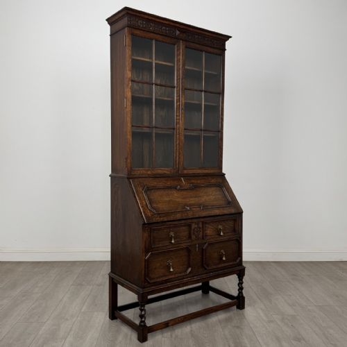 fig 8. A dark oak bureau bookcase with upper glazed doors, a fall-front desk flap, lower drawers, and turned barley twist legs.
