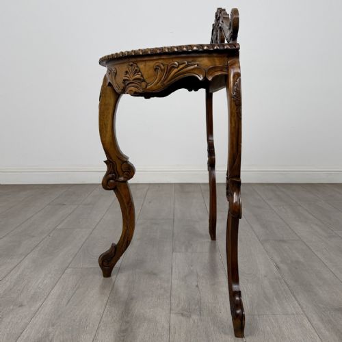 fig 2. A semicircular carved wooden demi-lune console table featuring cabriole legs, an ornate raised gallery back with carved floral motif, and a gadrooned top edge.