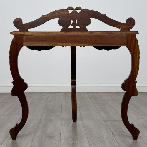 fig 3. A semicircular carved wooden demi-lune console table featuring cabriole legs, an ornate raised gallery back with carved floral motif, and a gadrooned top edge.
