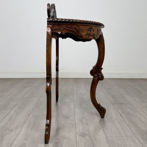 fig 4. A semicircular carved wooden demi-lune console table featuring cabriole legs, an ornate raised gallery back with carved floral motif, and a gadrooned top edge.