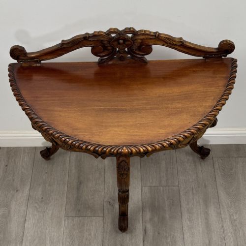 fig 6. A semicircular carved wooden demi-lune console table featuring cabriole legs, an ornate raised gallery back with carved floral motif, and a gadrooned top edge.