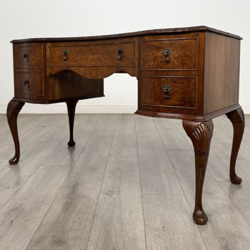 fig 1. A Queen Anne style burr walnut writing desk featuring a serpentine front, five drawers with brass handles, and carved cabriole legs.