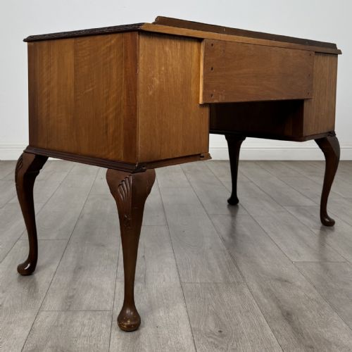 fig 3. A Queen Anne style burr walnut writing desk featuring a serpentine front, five drawers with brass handles, and carved cabriole legs.