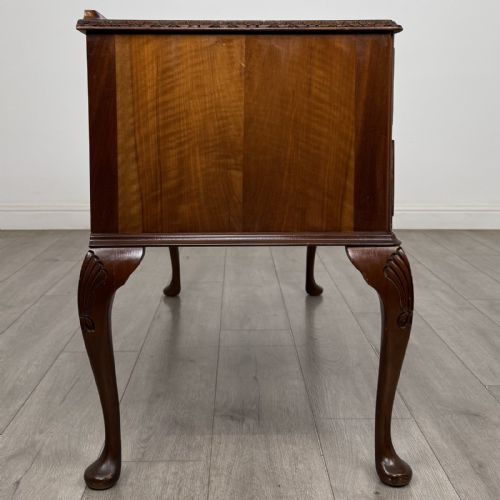 fig 6. A Queen Anne style burr walnut writing desk featuring a serpentine front, five drawers with brass handles, and carved cabriole legs.
