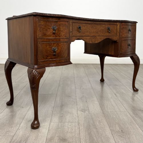 fig 7. A Queen Anne style burr walnut writing desk featuring a serpentine front, five drawers with brass handles, and carved cabriole legs.