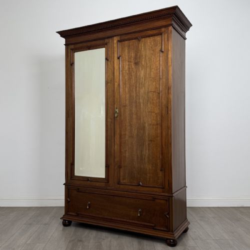 fig 1. An antique early 20th-century walnut double wardrobe featuring a full-length mirror door, panelled right door, geometric mouldings, and a single lower drawer.