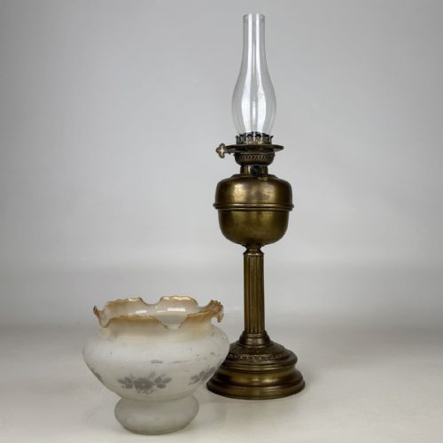 fig 1. An antique brass oil lamp featuring a reeded pedestal column, a clear glass chimney, and a frilled frosted glass shade decorated with floral etching.