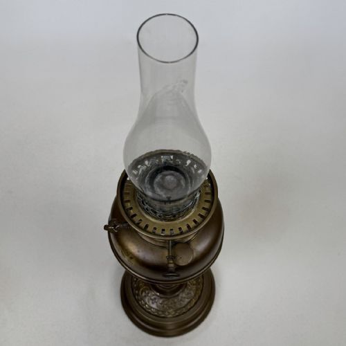 fig 2. An antique brass oil lamp featuring a reeded pedestal column, a clear glass chimney, and a frilled frosted glass shade decorated with floral etching.