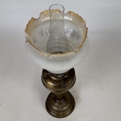 fig 4. An antique brass oil lamp featuring a reeded pedestal column, a clear glass chimney, and a frilled frosted glass shade decorated with floral etching.
