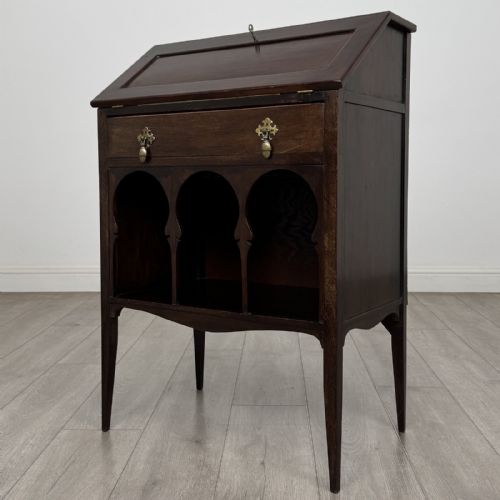 fig 1. An Edwardian dark mahogany bureau featuring a slant-front writing lid, a single drawer with brass drop handles, open lower compartment with arches, and tapered legs.