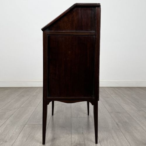 fig 2. An Edwardian dark mahogany bureau featuring a slant-front writing lid, a single drawer with brass drop handles, open lower compartment with arches, and tapered legs.