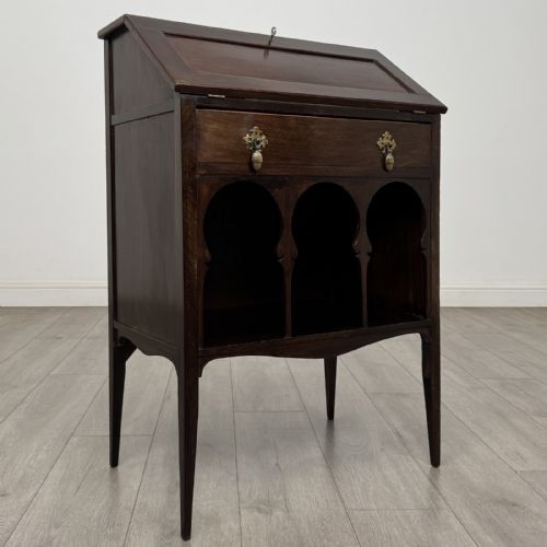 fig 7. An Edwardian dark mahogany bureau featuring a slant-front writing lid, a single drawer with brass drop handles, open lower compartment with arches, and tapered legs.
