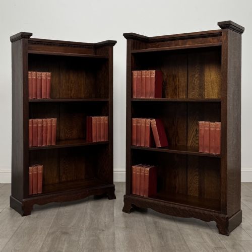 fig 1. A matching pair of dark oak Edwardian open bookcases featuring carved cornices, three shelves, and shaped plinth bases.