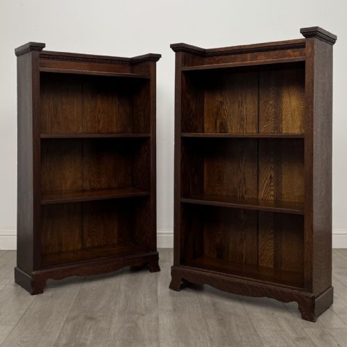 fig 2. A matching pair of dark oak Edwardian open bookcases featuring carved cornices, three shelves, and shaped plinth bases.