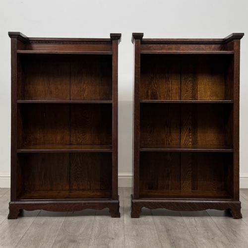 fig 3. A matching pair of dark oak Edwardian open bookcases featuring carved cornices, three shelves, and shaped plinth bases.