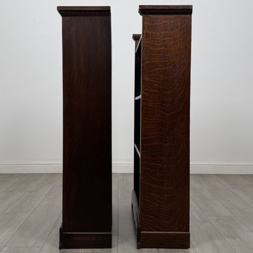 fig 4. A matching pair of dark oak Edwardian open bookcases featuring carved cornices, three shelves, and shaped plinth bases.