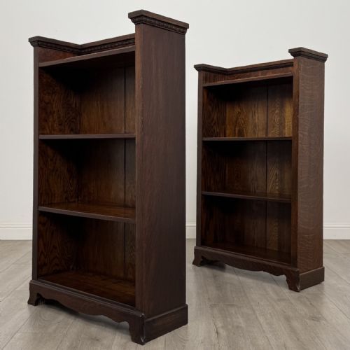 fig 5. A matching pair of dark oak Edwardian open bookcases featuring carved cornices, three shelves, and shaped plinth bases.