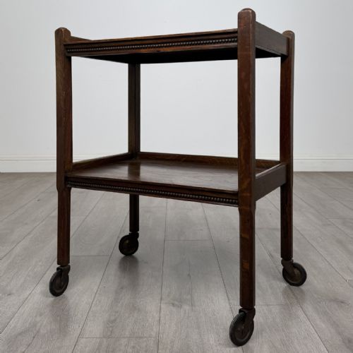 fig 1. A dark oak two-tier tea trolley featuring beaded moulding along the edges and small dark castors on four straight legs.