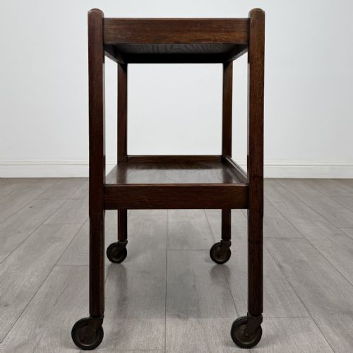 fig 2. A dark oak two-tier tea trolley featuring beaded moulding along the edges and small dark castors on four straight legs.