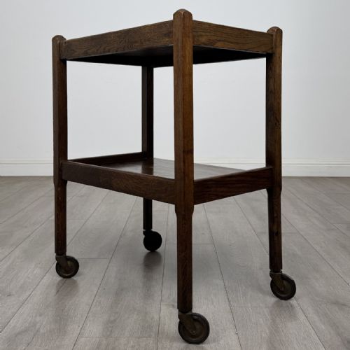 fig 5. A dark oak two-tier tea trolley featuring beaded moulding along the edges and small dark castors on four straight legs.
