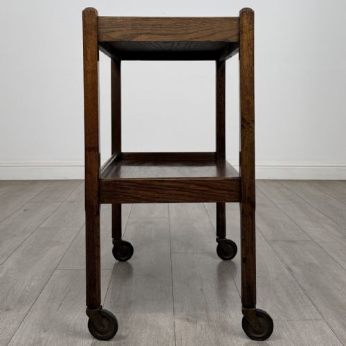 fig 6. A dark oak two-tier tea trolley featuring beaded moulding along the edges and small dark castors on four straight legs.