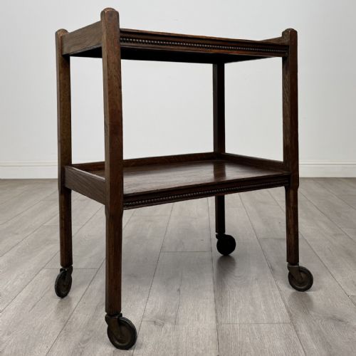 fig 7. A dark oak two-tier tea trolley featuring beaded moulding along the edges and small dark castors on four straight legs.