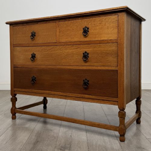 fig 1. An antique oak chest of drawers featuring two short drawers above two long drawers, metal drop handles, turned legs, and a lower stretcher rail.