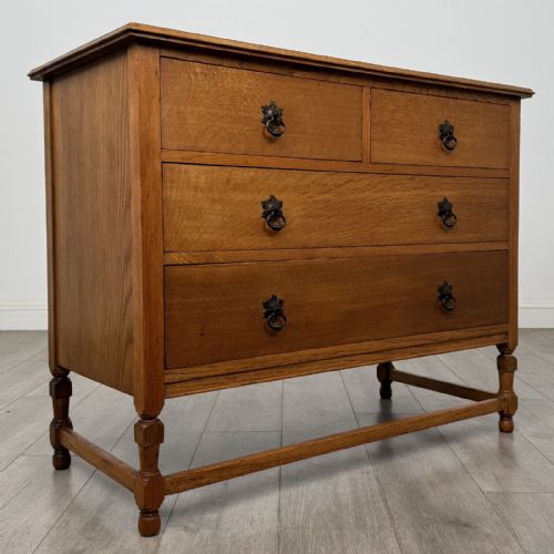 fig 7. An antique oak chest of drawers featuring two short drawers above two long drawers, metal drop handles, turned legs, and a lower stretcher rail.