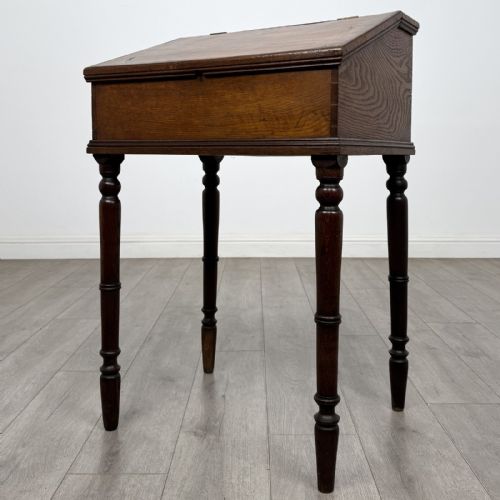 fig 2. A small dark oak Victorian clerks desk with a sloped hinged lid raised on tall turned legs.