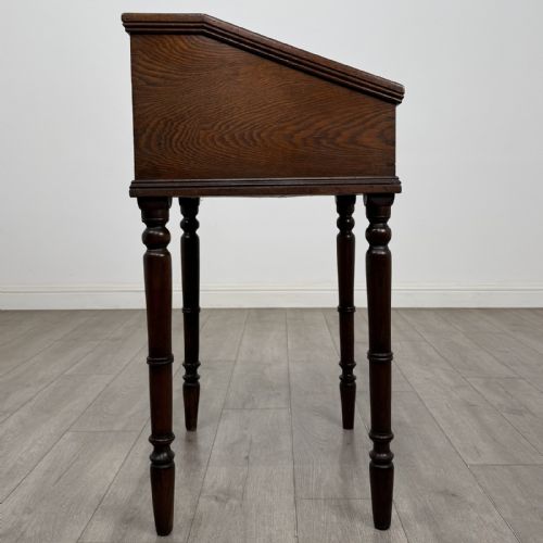 fig 7. A small dark oak Victorian clerks desk with a sloped hinged lid raised on tall turned legs.