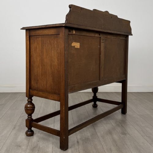 fig 4. A Jacobean style oak sideboard featuring two drawers, carved door panels, metal drop handles, and turned cup and cover legs connected by low stretchers.