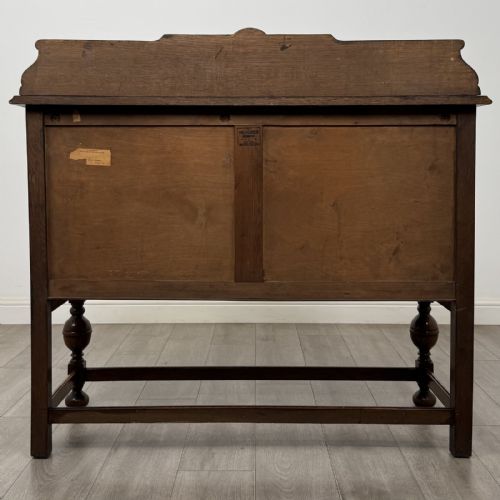 fig 5. A Jacobean style oak sideboard featuring two drawers, carved door panels, metal drop handles, and turned cup and cover legs connected by low stretchers.