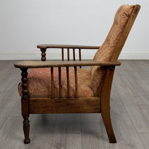 fig 1. An Arts and Crafts oak reclining armchair with wide armrests, turned front legs, vertical side spindles, and patterned terracotta upholstered cushions.