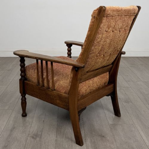 fig 2. An Arts and Crafts oak reclining armchair with wide armrests, turned front legs, vertical side spindles, and patterned terracotta upholstered cushions.